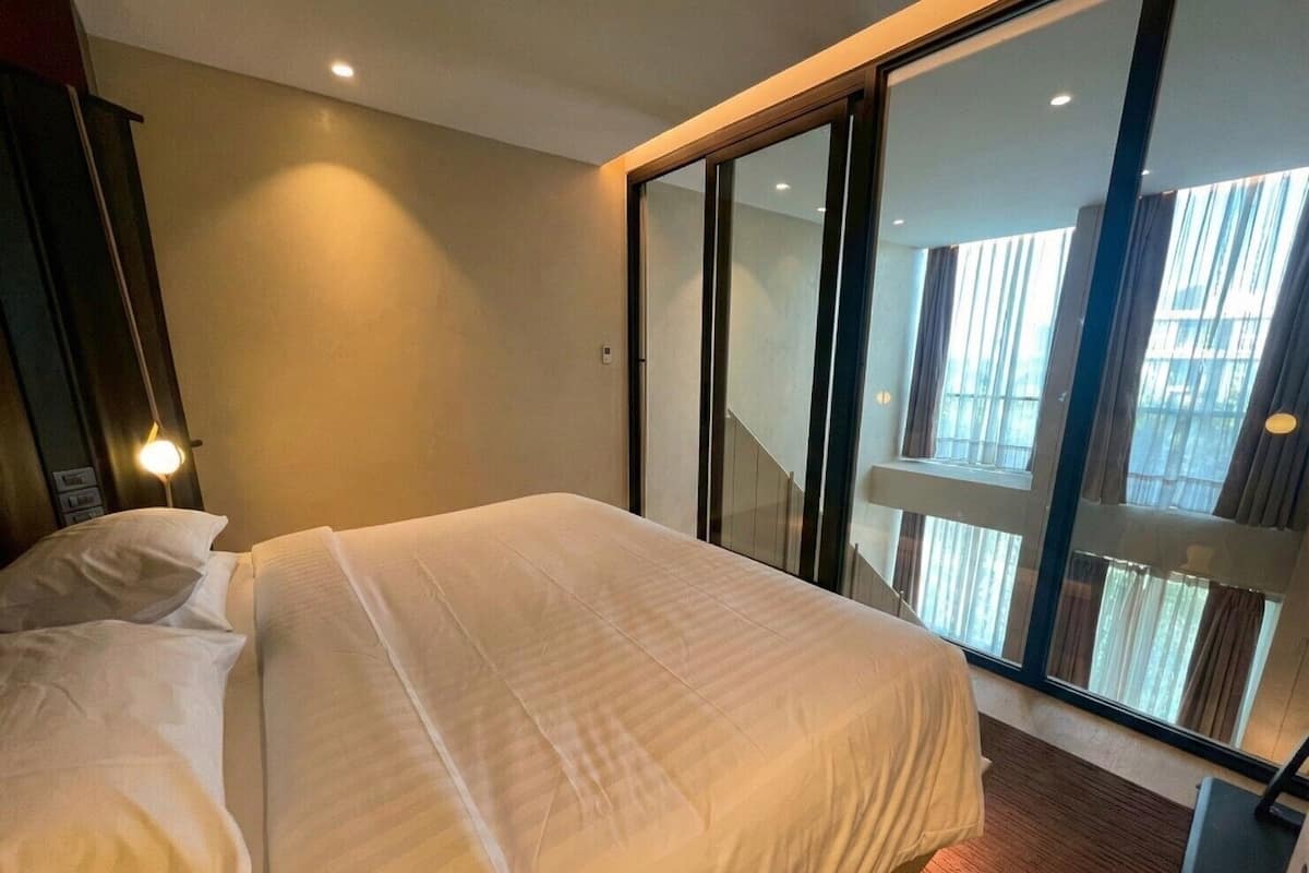 Hotellihuone, jossa on suuri sänky, yöpöytä, lamppu ja liukuovet, jotka johtavat parvekkeelle.
