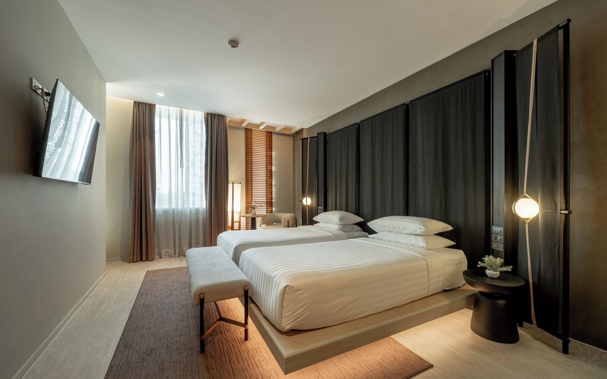 A modern hotel room with two beds, a flat-screen TV, a desk, and a large window with curtains.