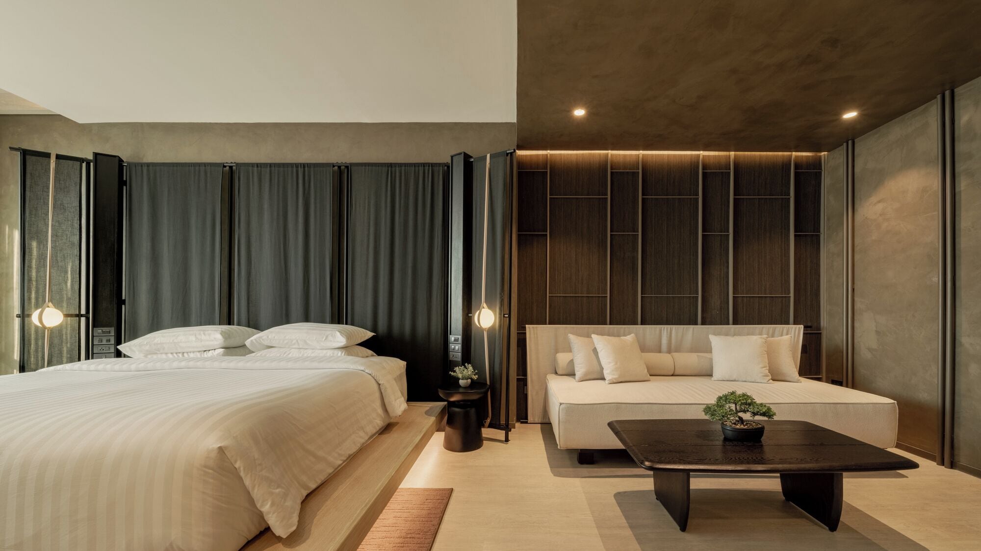 A modern hotel room with a large bed, a sofa, a coffee table, and a small plant.