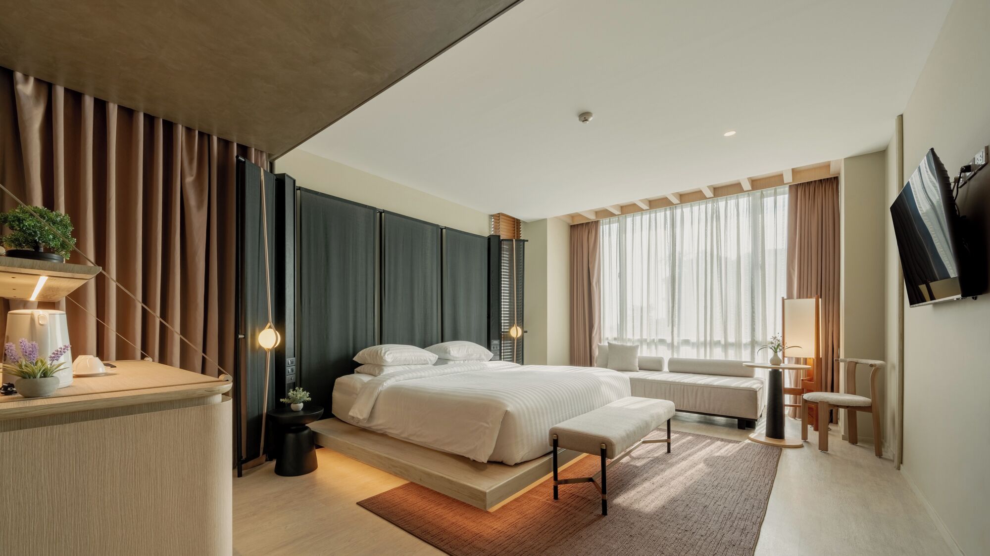 Una habitación de hotel moderna con una cama grande, mesitas de noche, un escritorio y un televisor montado en la pared.