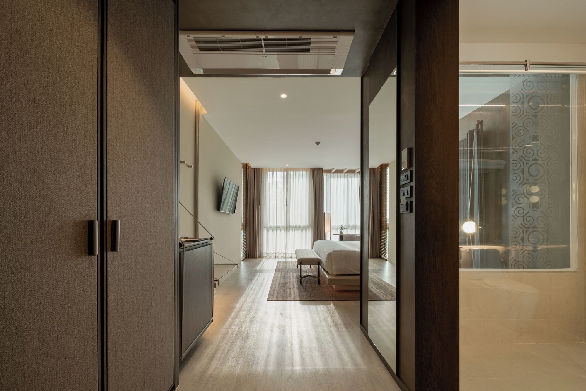 A modern hotel room with a large bed, a desk, and a view of the city through floor-to-ceiling windows.