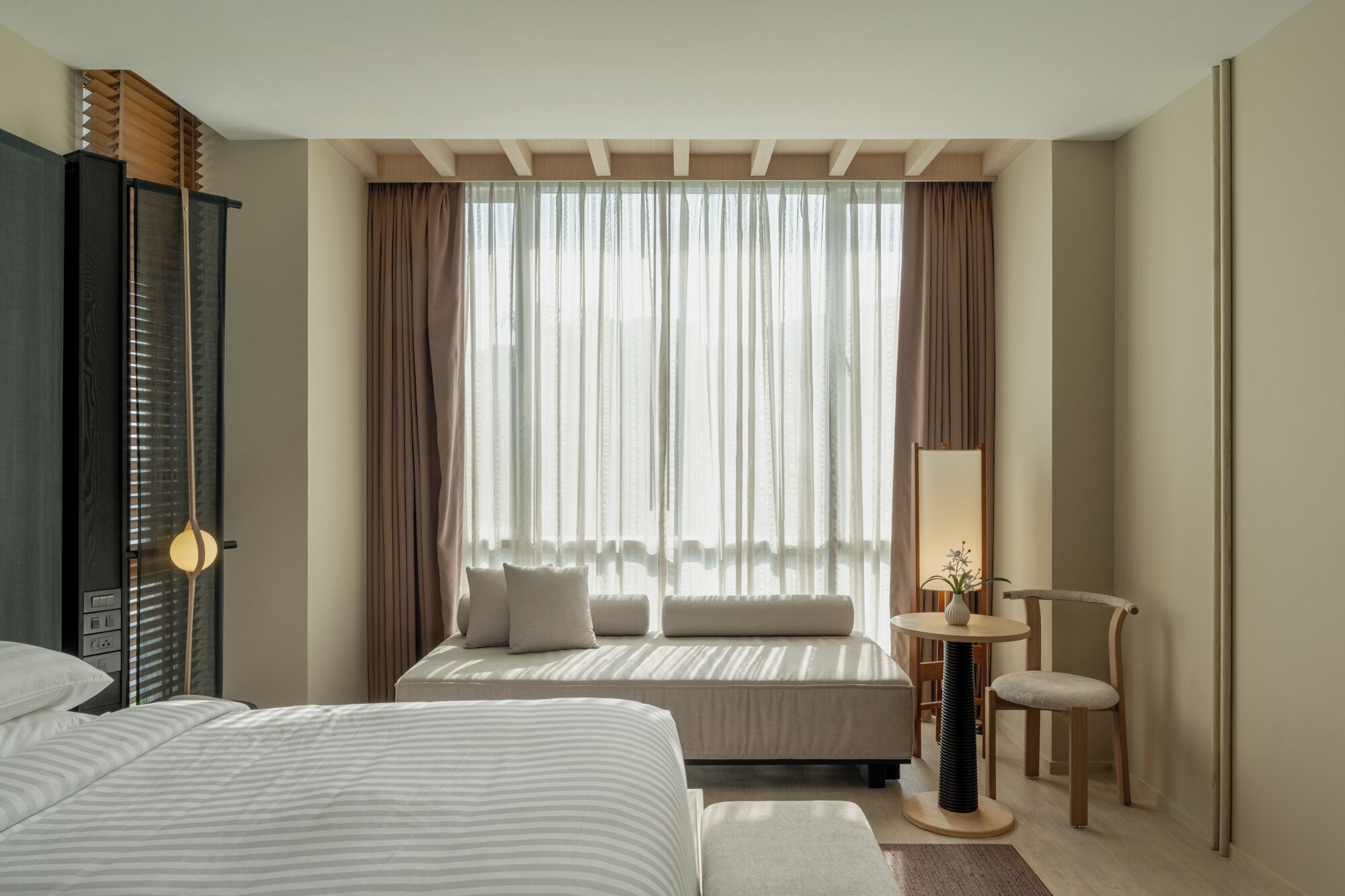 A hotel room with a bed, a sofa, a small table with a lamp, and a chair.