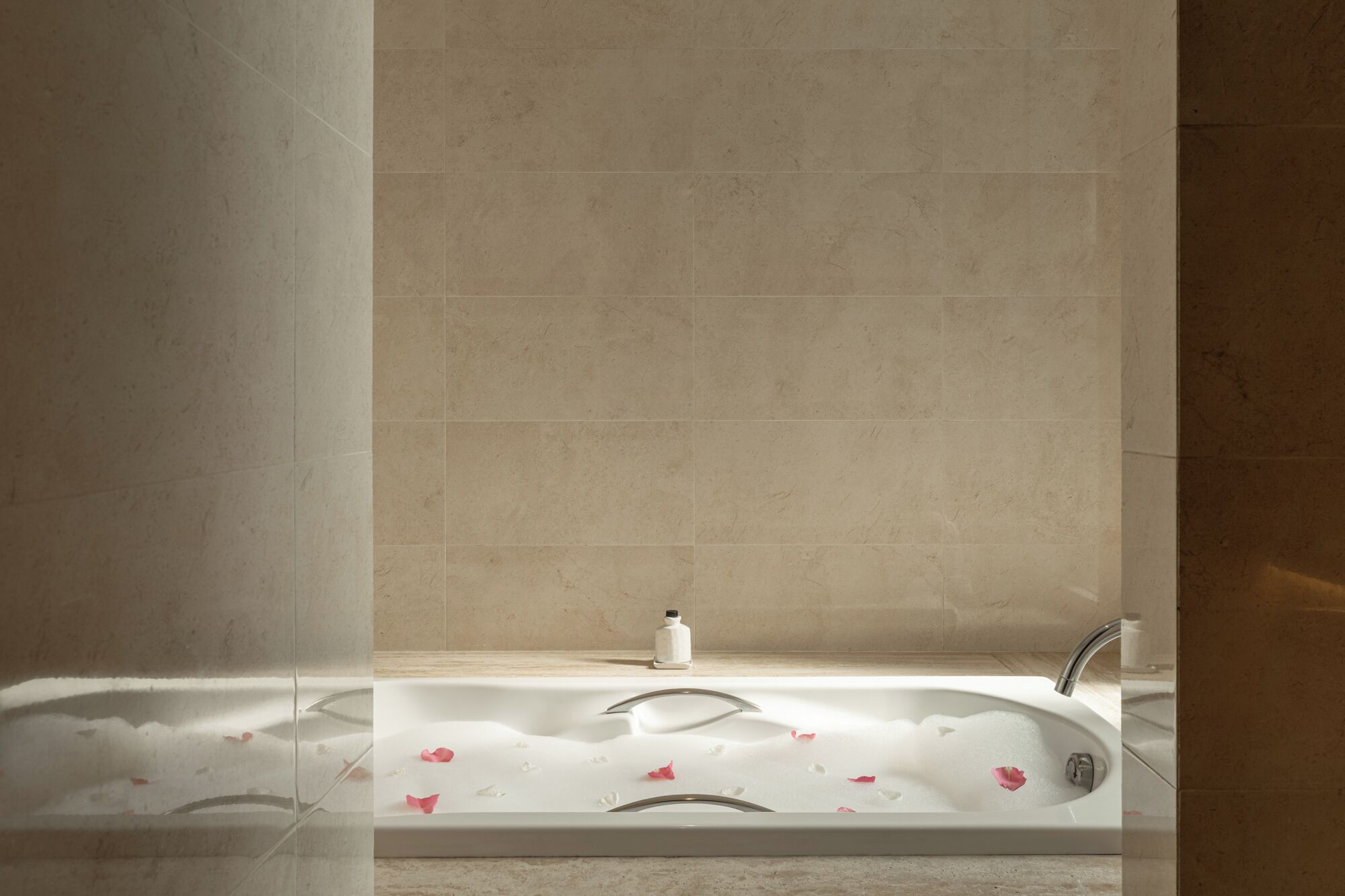 A bathroom with a bathtub, a white bottle, and rose petals on the floor.
