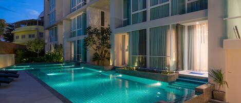 A modern hotel with a swimming pool, large windows, and a well-lit exterior.