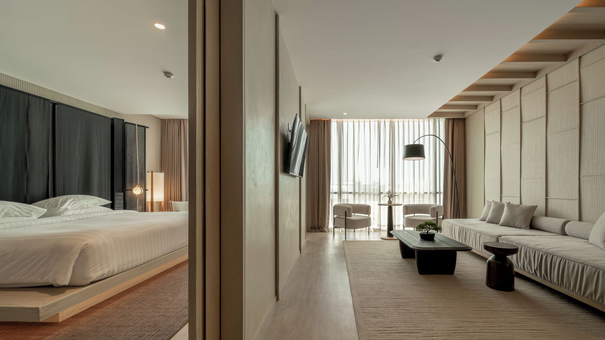 A modern hotel room with a large bed, a sofa, a coffee table, and a dining area with chairs.