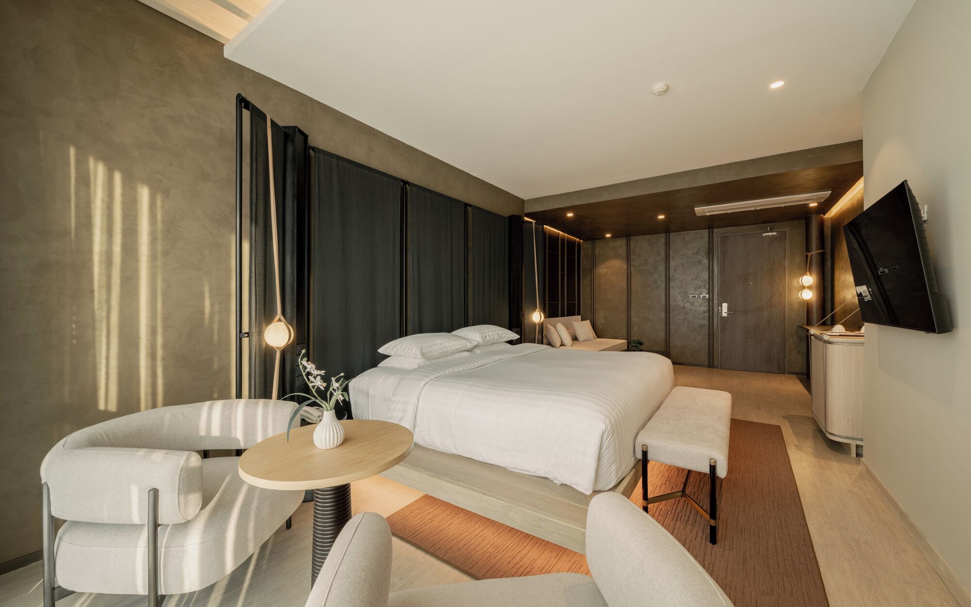 A modern hotel room with a large bed, a seating area with a table, and a TV mounted on the wall.
