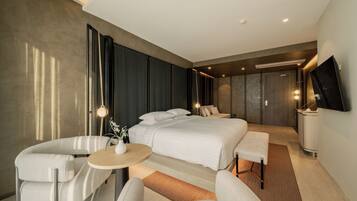 Una habitación de hotel moderna con una cama grande, una zona de estar con una mesa y un televisor montado en la pared.