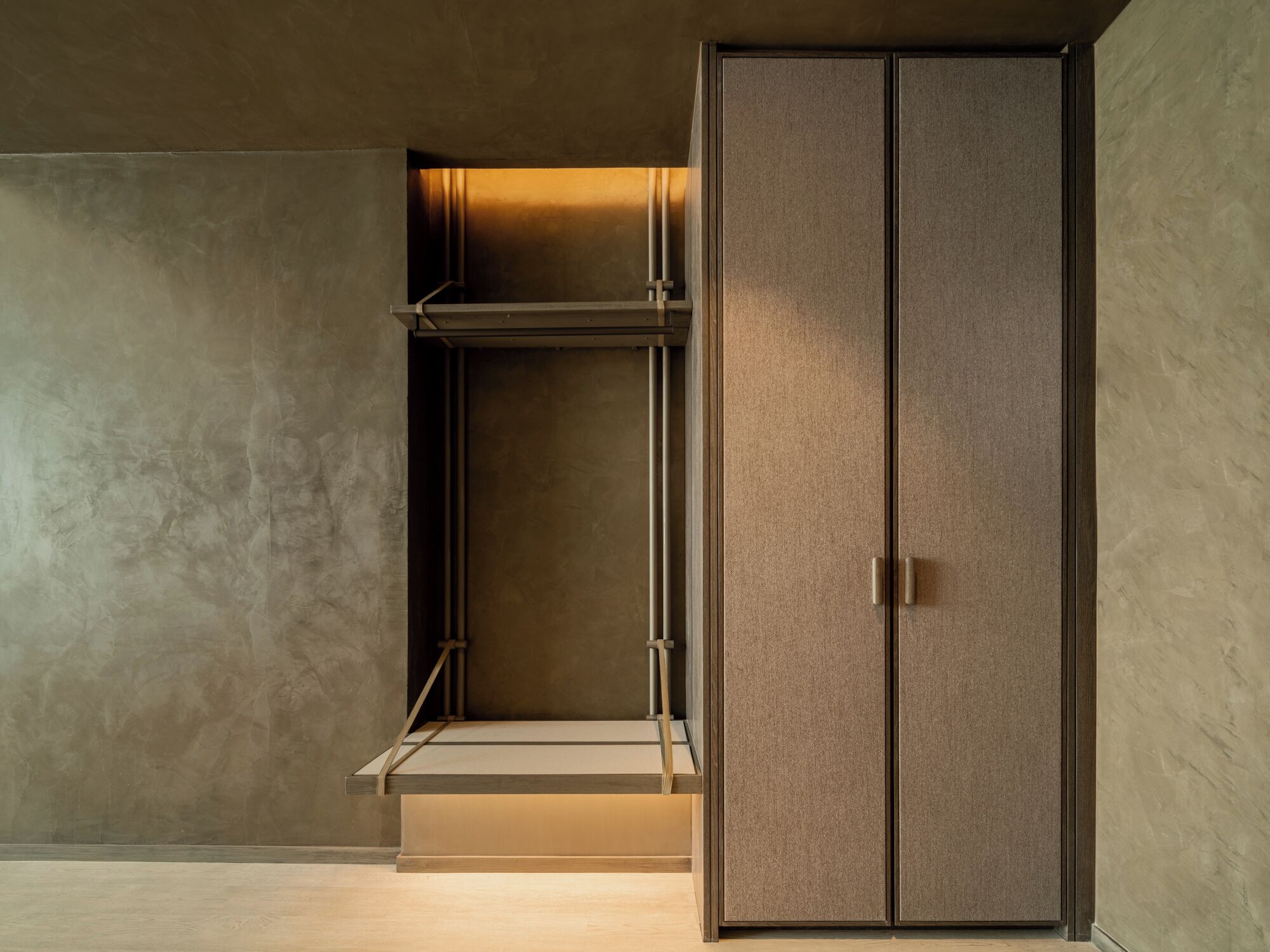 A minimalist room with a large wardrobe, a metal shelf unit, and a concrete wall.