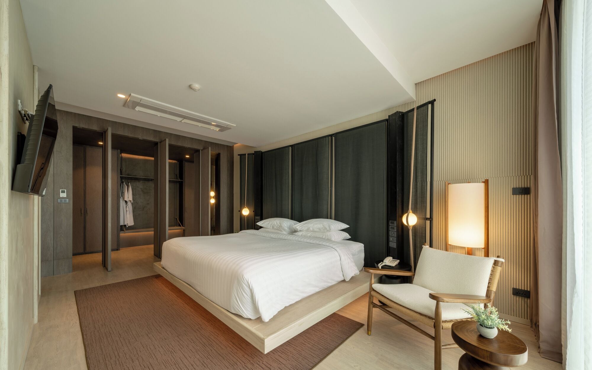 Une chambre d’hôtel moderne, dotée d’un grand lit, d’une chaise, d’un bureau et d’un téléviseur fixé au mur.