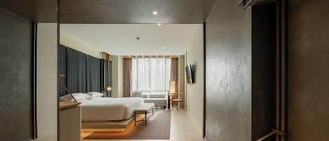 A modern hotel room with a large bed, a desk, and a view of the city.