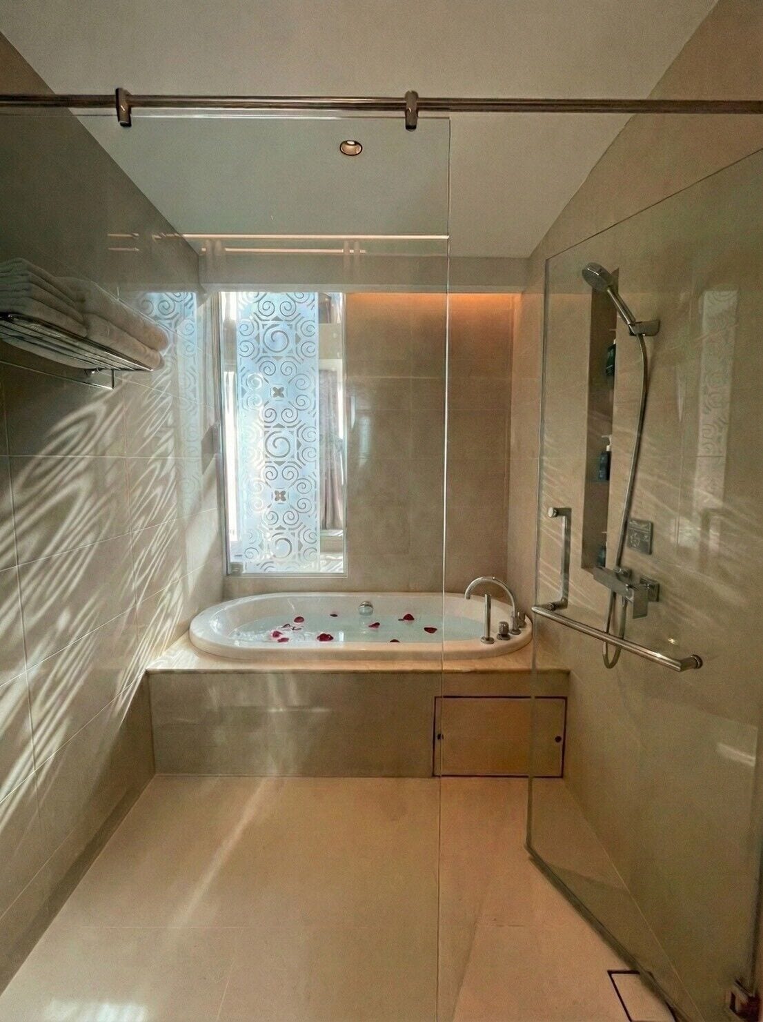 A modern bathroom with a glass-enclosed shower, a freestanding bathtub, and a window with decorative curtains.