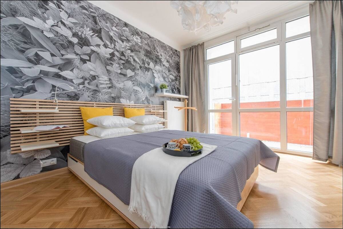 A modern bedroom with a large bed, a wooden headboard, and a grey floral wall.