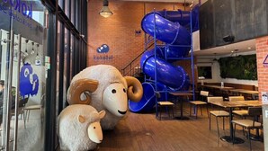Interior de un restaurante con pared de ladrillo, un tobogán azul y esculturas grandes de ovejas.