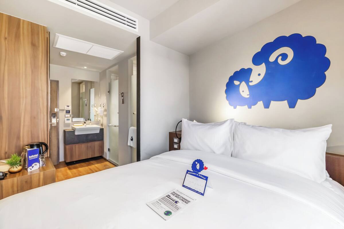 A hotel room with a bed, a bathroom, and a wall with a sheep decoration.