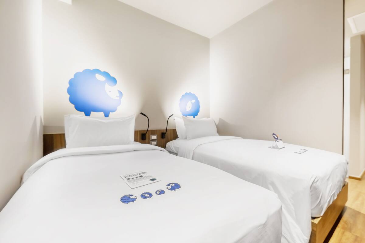 A hotel room with two single beds, each with a white bedspread and a small table with a phone and papers.