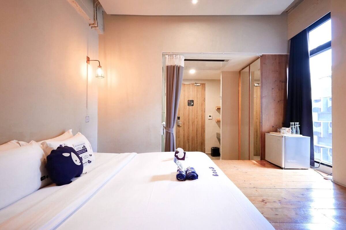 A hotel room with a bed, a suitcase, a small table with glasses, and a view of the outside.