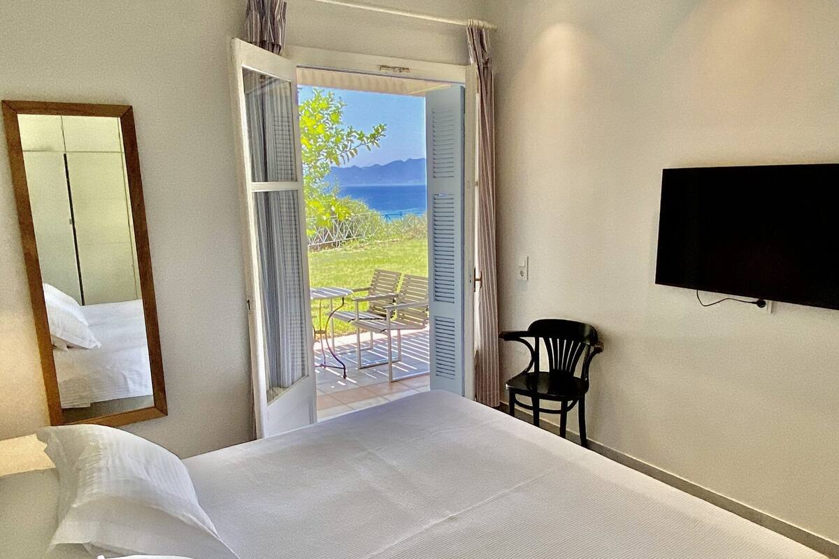 Habitación de hotel con cama, una silla, televisión y balcón con vista al mar.
