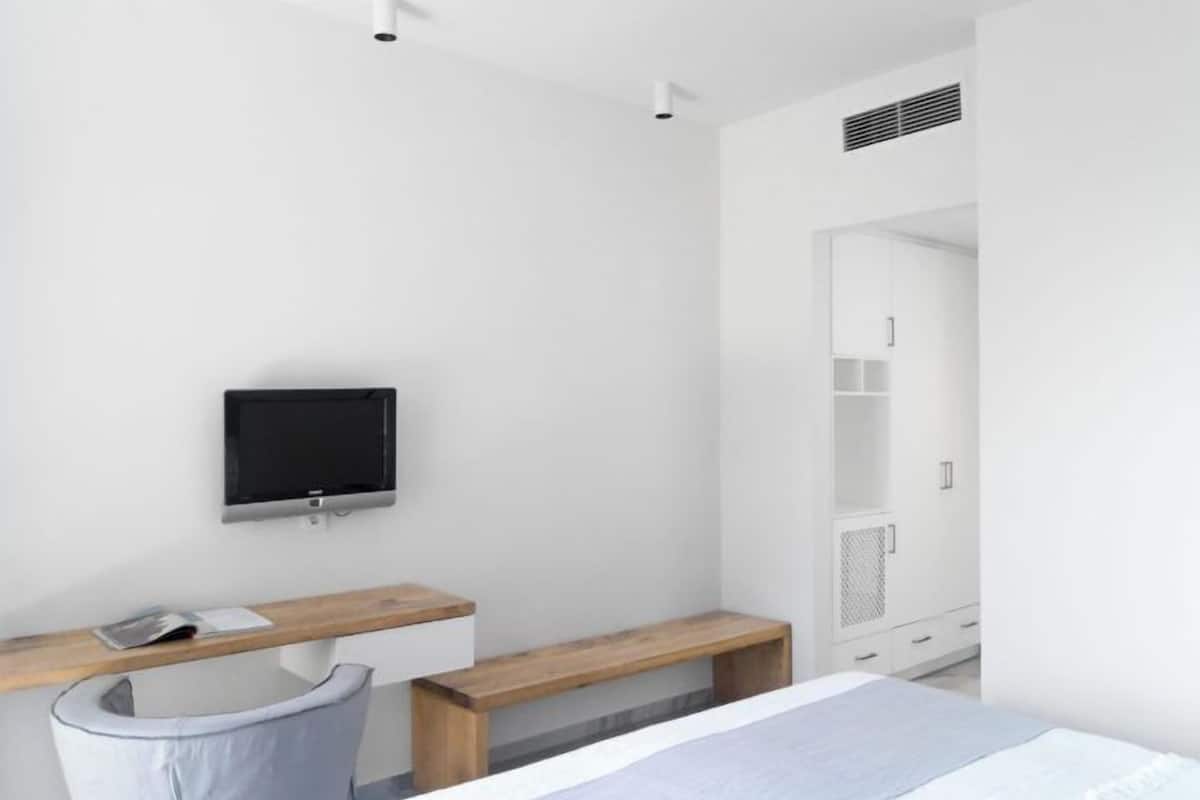 Una habitación de hotel moderna con una cama, un escritorio con silla, un televisor y un armario.
