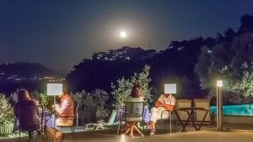 Un área de estar al aire libre con mesas y sillas bajo un cielo nocturno con luna visible.