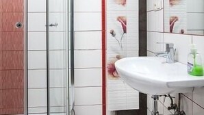 A bathroom with a glass shower enclosure, a white sink, and decorative floral tiles. - EchoDom 5 Apartments Florianska (Kraków)