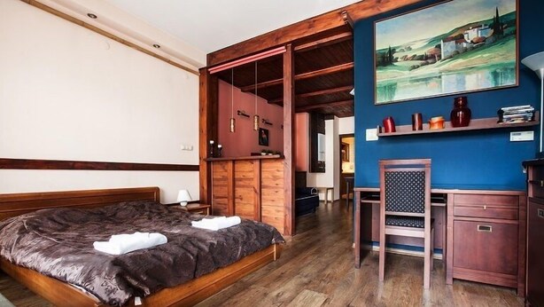 A bedroom with a wooden bed, a desk, and a chair. There is a painting on the wall and a shelf with decorative items. - EchoDom 5 Apartments Florianska (Kraków)