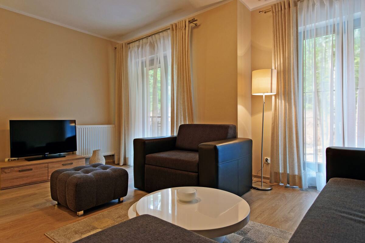 Ein modernes Wohnzimmer mit Fernseher, braunem Ledersessel, weißem Couchtisch und einer Couch.