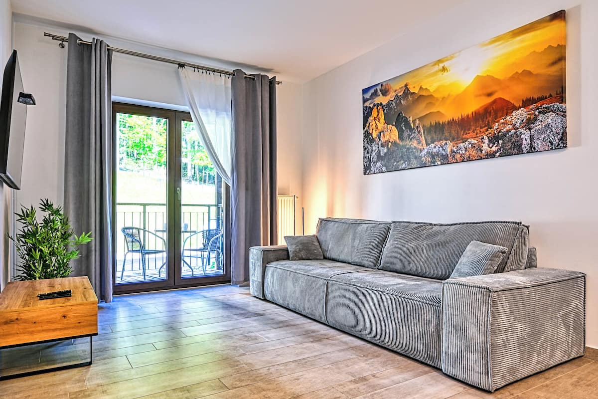 Ein modernes Wohnzimmer mit einer Couch, einem Holztisch, einer Topfpflanze und einem großen Gemälde von einer Berglandschaft.