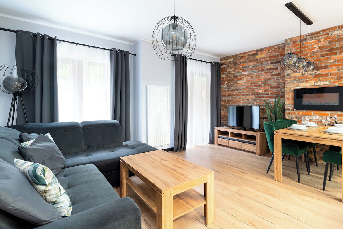 Ein modernes Wohnzimmer mit Sofa, Couchtisch, Esstisch mit Stühlen, Fernseher und einer Ziegelwand.