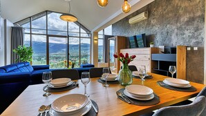A dining area with a view of mountains, a blue sofa, and a wooden dining table set for four. - Sun & Snow Resort Sudety (Szklarska Poreba)