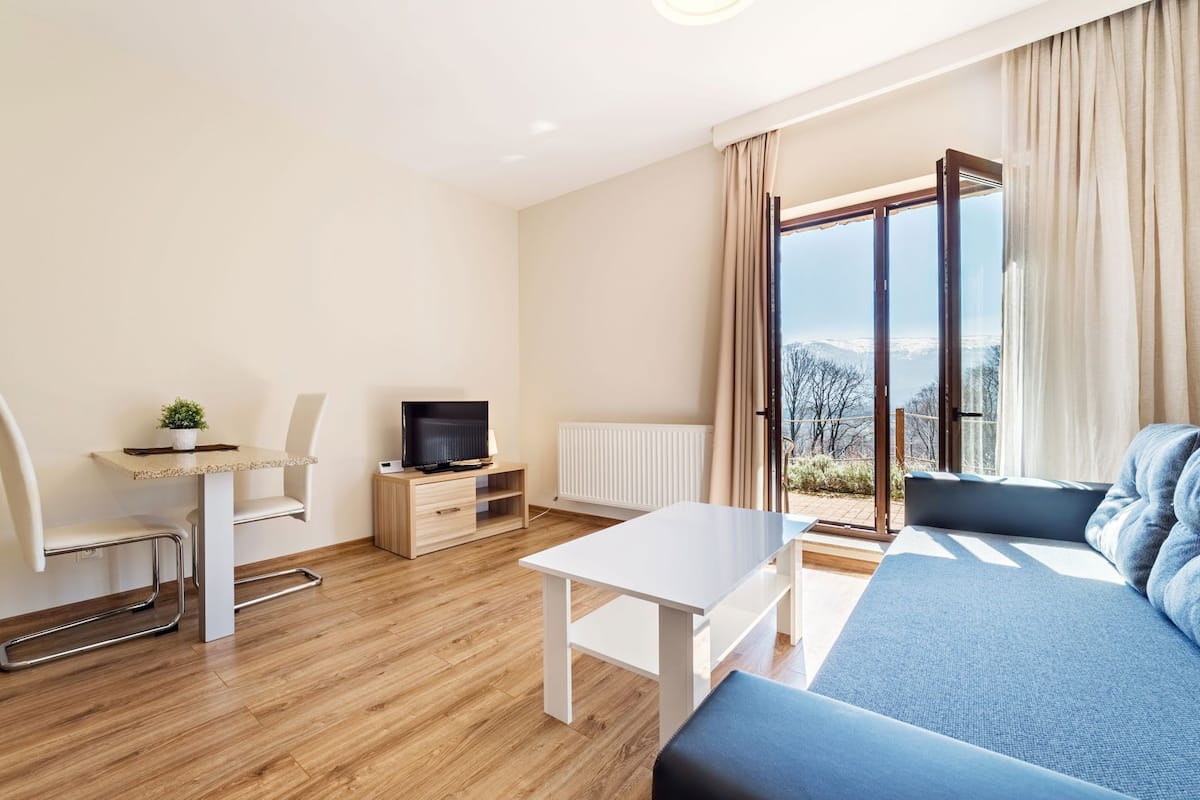 Ein modernes Wohnzimmer mit einer Couch, einem Fernseher, einem kleinen Tisch und einem Sessel.
