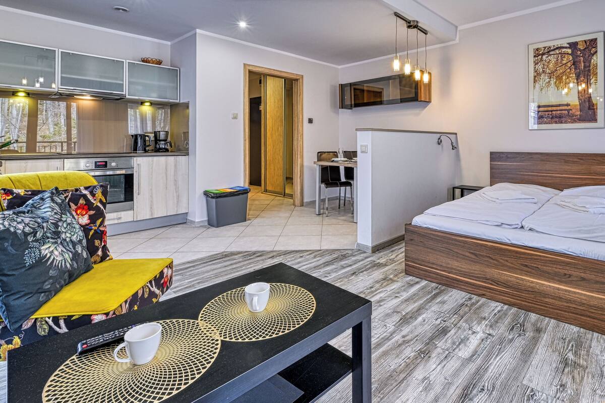 Ein modernes Hotelzimmer mit einem hölzernen Bett, einer kleinen Küchenzeile und einem Esstisch.