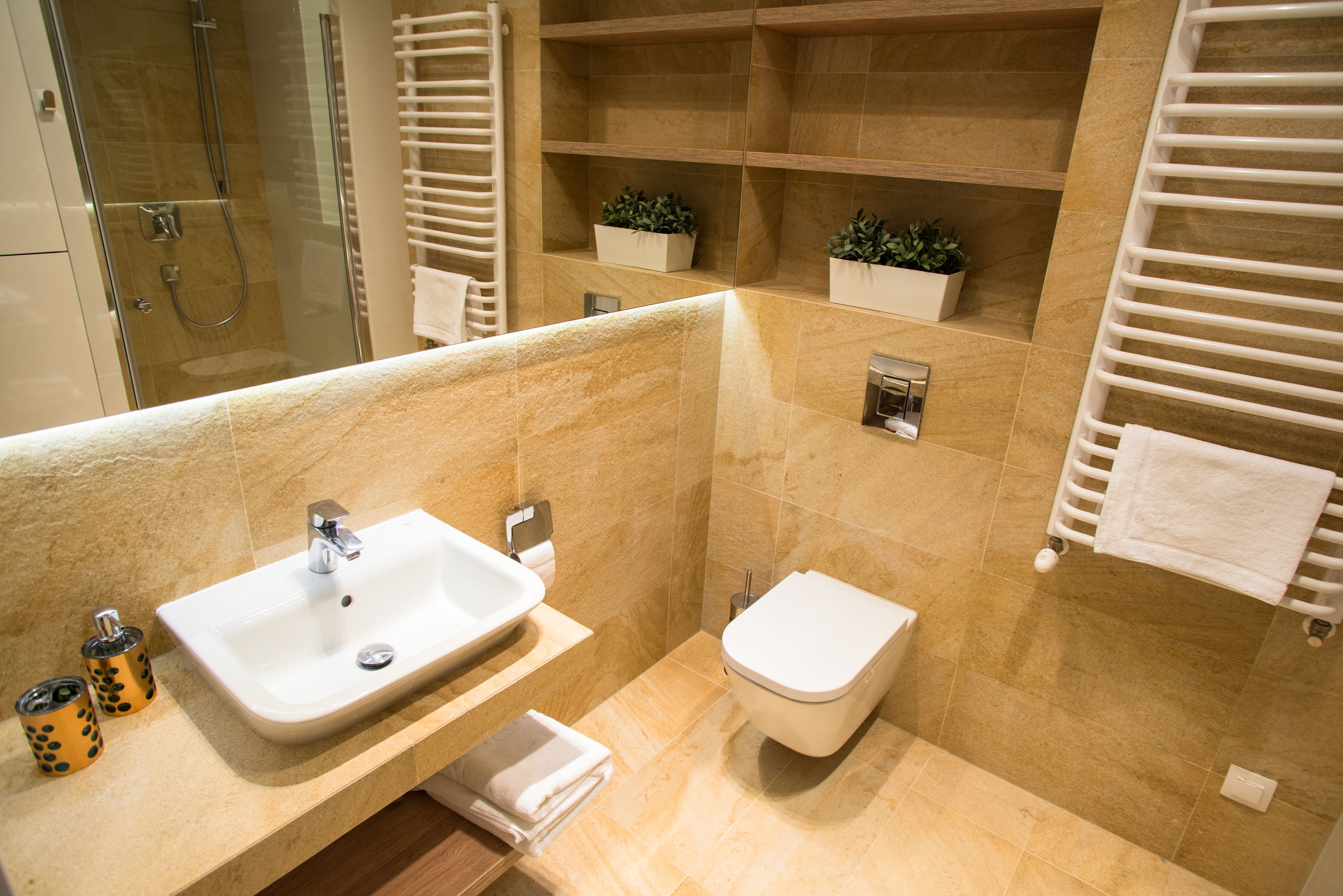 A modern bathroom with a sink, toilet, and shower. There are shelves with plants and a towel rack.