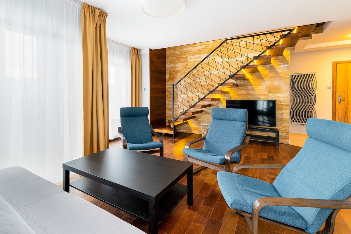 Ein modernes Wohnzimmer mit einer Couch, zwei Sesseln, einem Couchtisch und einer Treppe mit Holzausstattung.