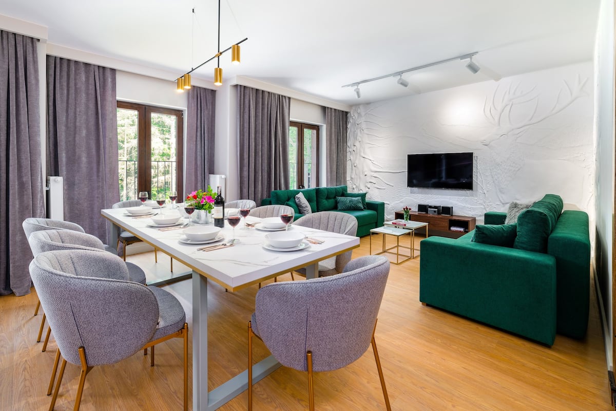 Ein modernes Wohnzimmer mit Essbereich, grünen Sofas, einem Flachbildfernseher und Holzboden.
