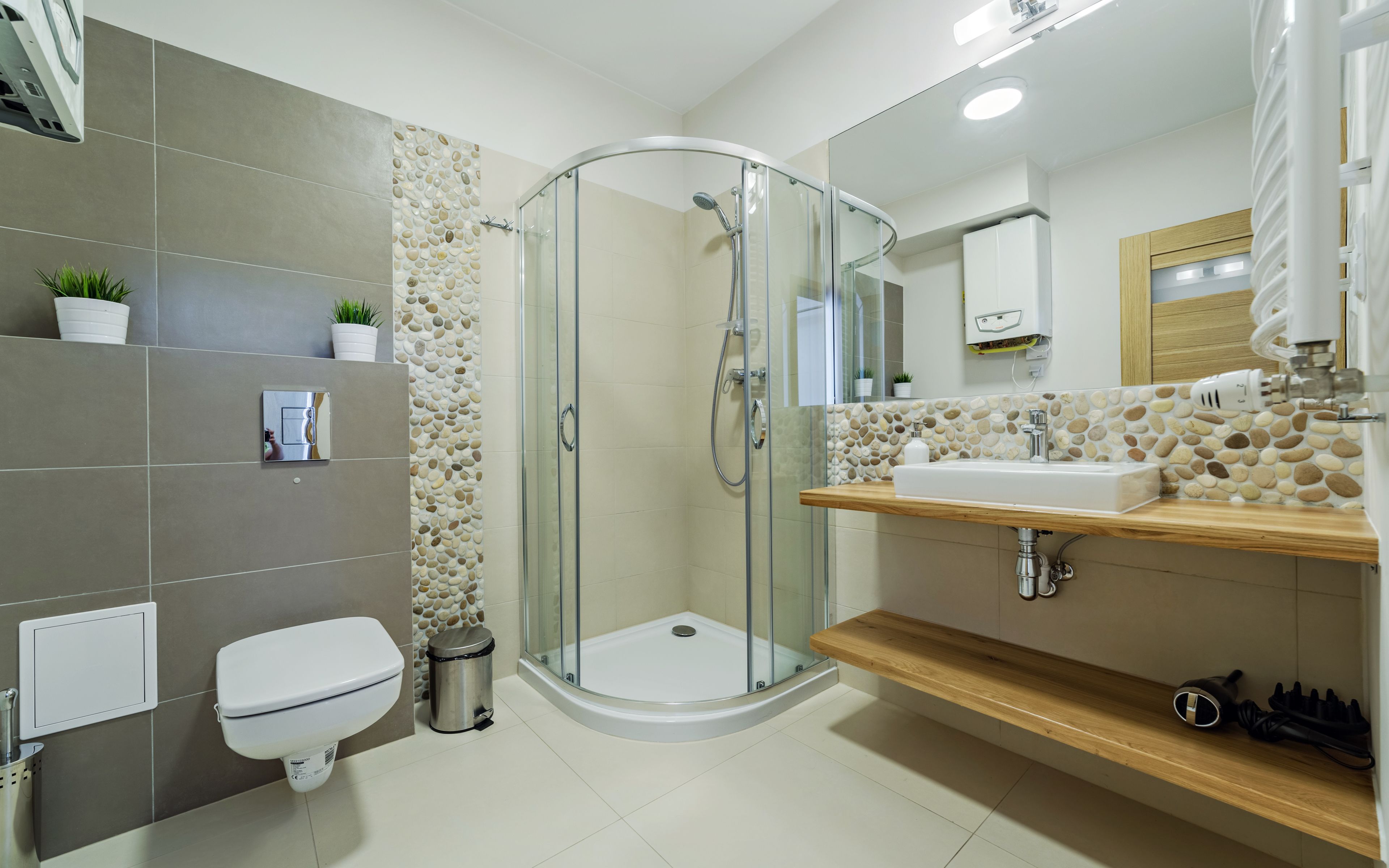 Een moderne badkamer met een douchecabine van glas, een toilet, een prullenbak en een wastafel met een houten aanrechtblad.