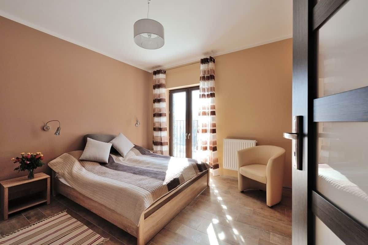Ein Schlafzimmer mit Bett, Nachttisch, Sessel und Blick durch ein Fenster.
