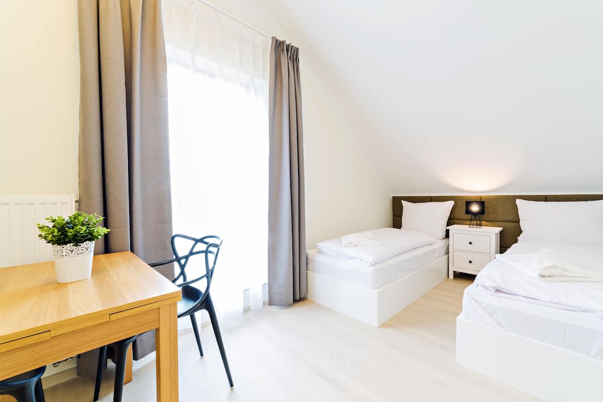 Ein Hotelzimmer mit Holztisch, zwei Betten, einem Nachttisch, einer Lampe und einem Topfpflanzen.