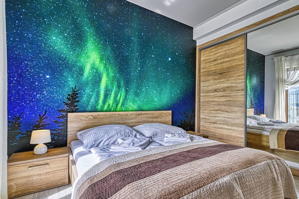 Ein Schlafzimmer mit Wandgemälde eines Sternenhimmels, einem großen Spiegel und Blick auf ein Gebirge.