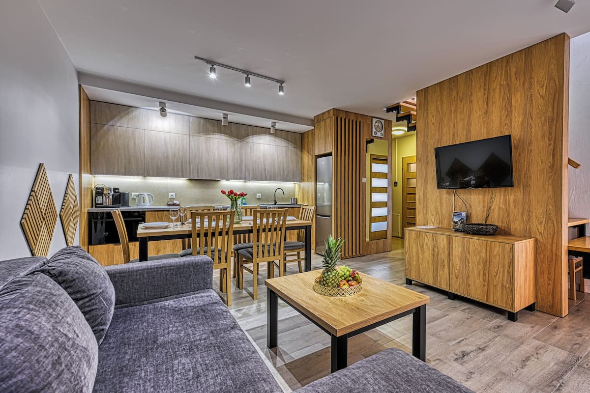Ein modernes Wohnzimmer mit einer Couch, einem Couchtisch und einem an einer Holzwand montierten Fernseher.