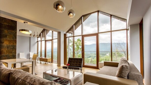 A spacious living room with a large window offering a mountain view, a modern sofa, a coffee table, and a dining area with a view. - Sun & Snow Resort Sudety (Szklarska Poreba)