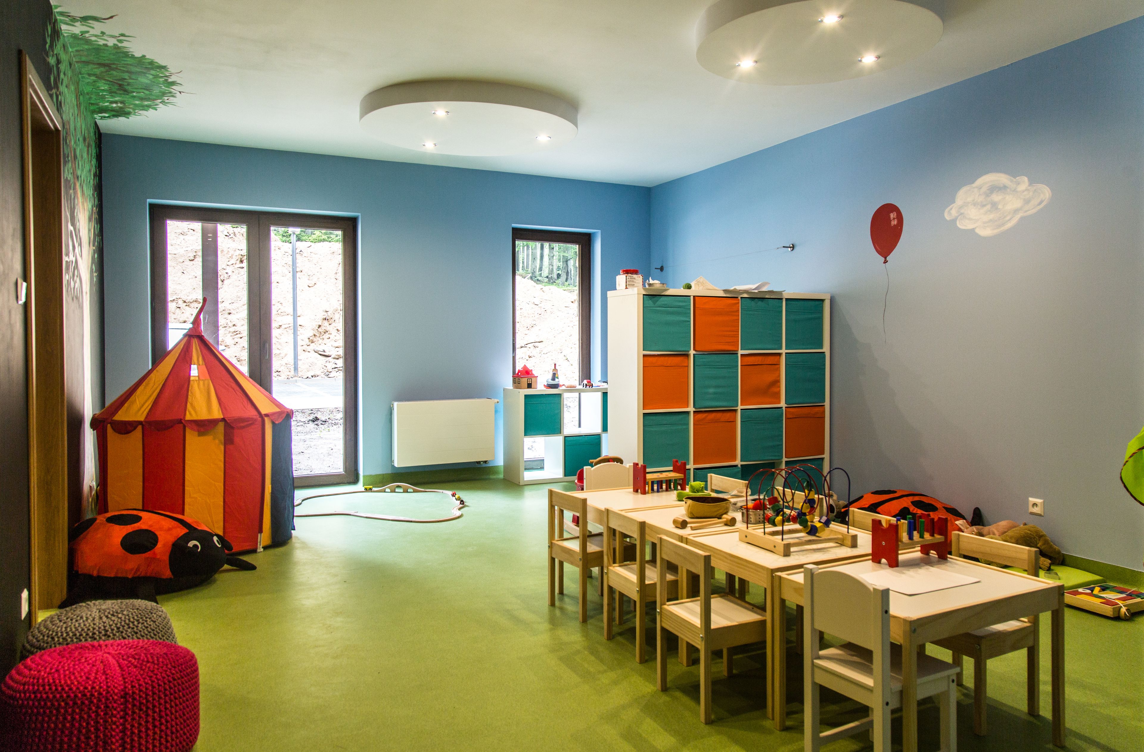 Een kinderspeelruimte met een grote tent, een lieveheersbeestje-kussen en een tafel vol speelgoed.