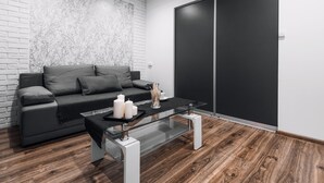 A modern living room with a grey sofa, a glass coffee table, and a black wardrobe.