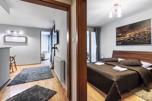 Ein Hotelzimmer mit Bett, Fernseher, einem Gemälde und Blick auf die beleuchtete Stadt.
