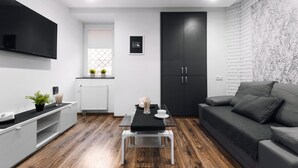 A modern living room with a grey sofa, a black TV mounted on the wall, a black cabinet, and a wooden floor.