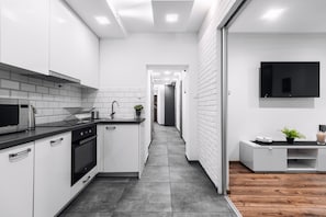 A modern kitchen with white cabinets, a black countertop, and a built-in oven. - EchoDom 7 Apartments Brzozowa (Kraków)