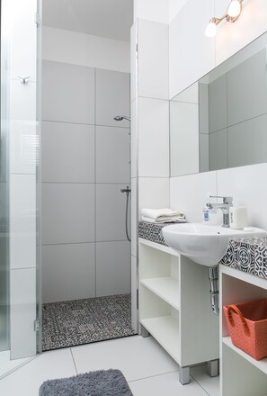 Ein modernes Badezimmer mit Duschkabine aus Glas, weißen Fliesen, einem Waschbeckenbereich mit Muster und einem Spiegel über dem Waschbecken.