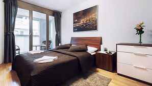 A modern bedroom with a large bed, a nightstand, a dresser, a window with curtains, and a cityscape painting on the wall.