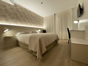 A modern bedroom with a large bed, bedside lamps, a desk, and a flat-screen TV mounted on the wall. - Hostal Paris (Valladolid)