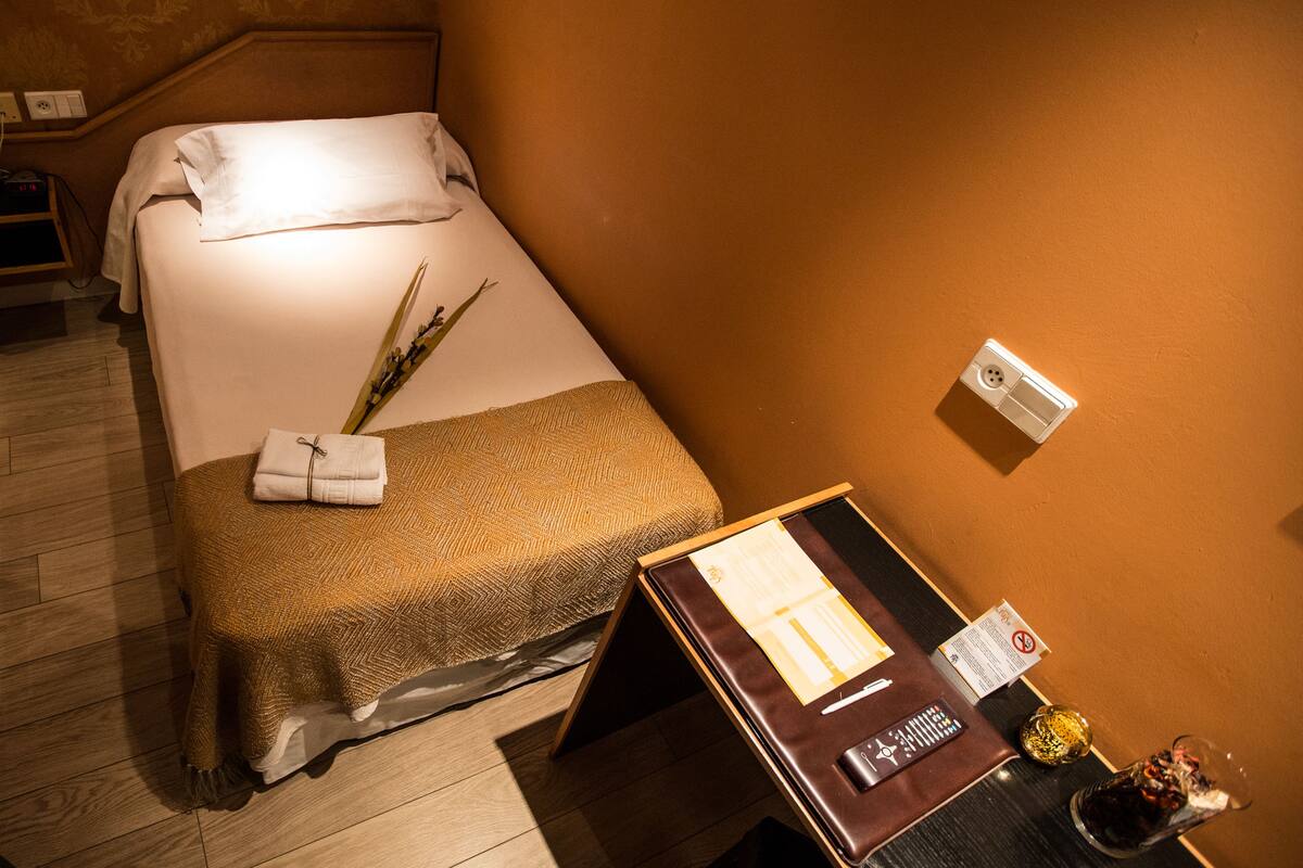 A hotel room with a bed, a bedside table with a remote control, a glass of water, and a small decorative item.
