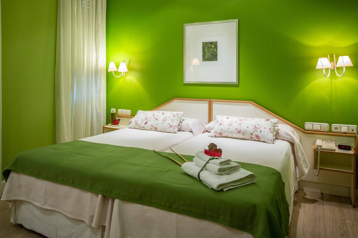 A hotel room with a large bed, green walls, two bedside tables with lamps, and a framed picture on the wall.